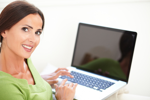Attractive woman looking over her shoulder at the camera while using a laptop - focus on foreground
