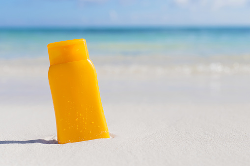 Yellow sunscreen lotion bottle on the beach (placed in white sand)