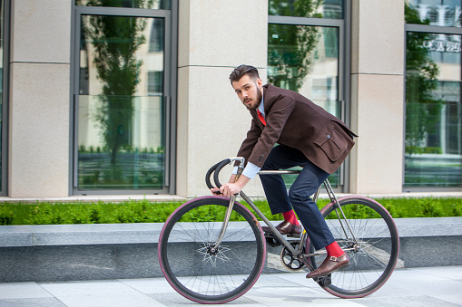Handsome businessman in a jacket riding on his bicycle on city streets. The concept of the modern lifestyle of young men