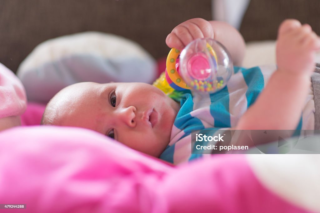 Baby playing with toy rattle lying on back Cute baby playing with holding toys 0-11 Months Stock Photo