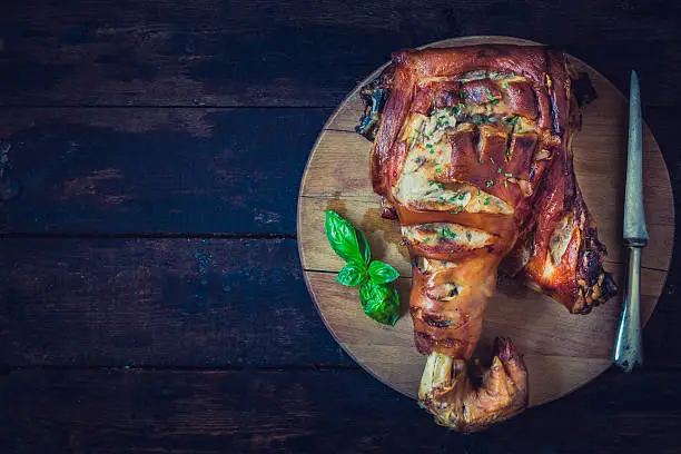 Roasted whole pork leg on wooden background with blank space on the left side