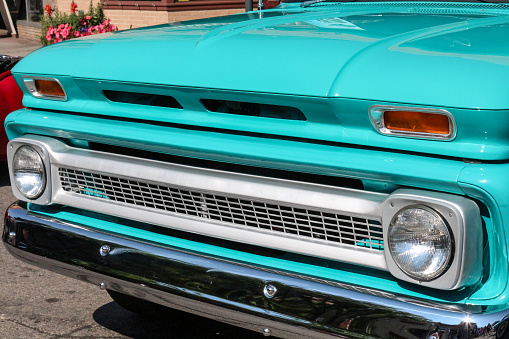 Image of the front of a 1960's vintage collectible truck.  The image has no people and shows both headlights on the old vehicle.  The antique has a metal grill and is painted bright turquoise.