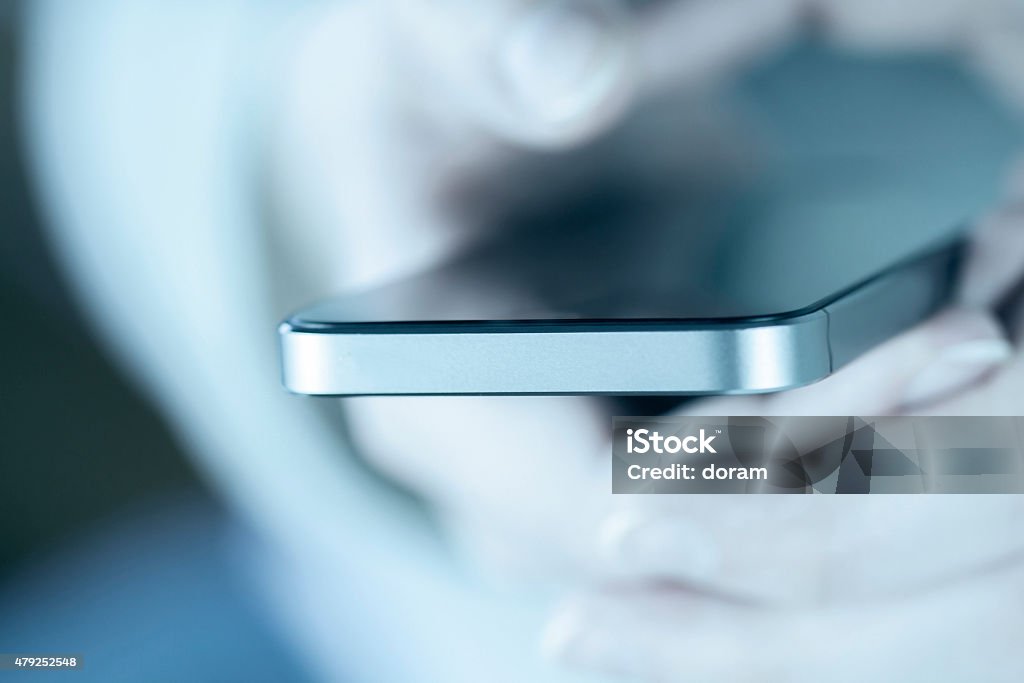 Woman texting holding her smartphone Woman texting, holding her smartphone, blue toning 2015 Stock Photo