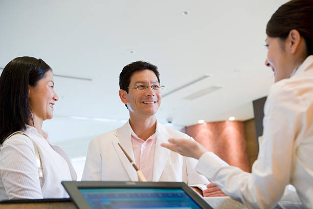 Husband and wife talking with hotel staff at  front desk stock photo