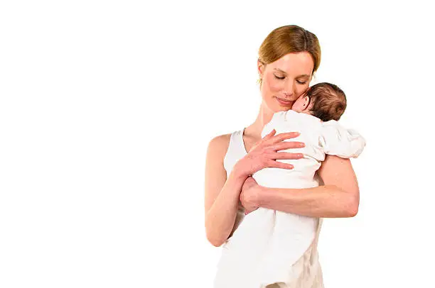 An adult woman with white shirt also has a white-clad sweet infant tenderly in her arms, isolated against a white background.