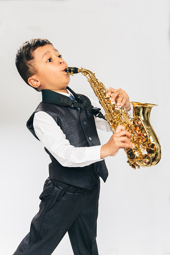 6 years old boy plays saxophone at studio, side view