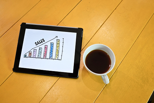 Hand drawing Sales Growth Graph on digital tablet screen with cup of black coffee