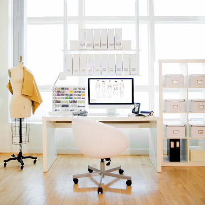 Design studio with fashion illustration designs on computer monitor with mannequin, fabric samples and no people.