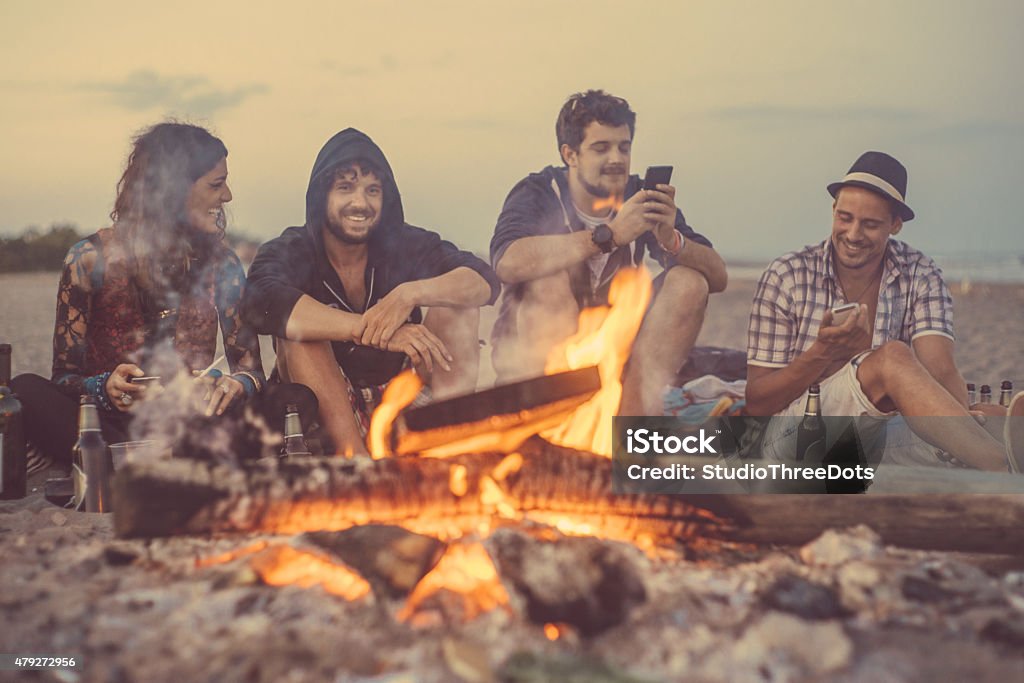 friends sitting around a camp fire happy friends sitting around a camp fire near the beach in early morning Campfire Stock Photo