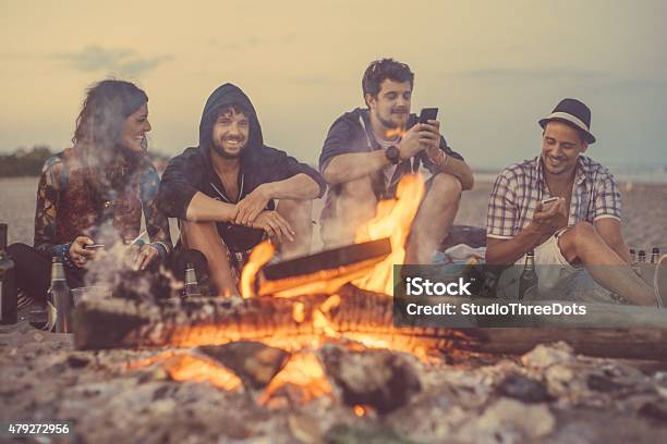 Friends Sitting Around A Camp Fire Stock Photo - Download Image Now - Campfire, Friendship, Using Phone