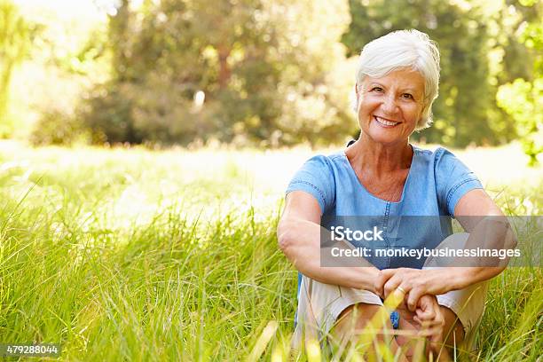 Senior Woman Sitting On Grass Relaxing Smiling To Camera Stock Photo - Download Image Now