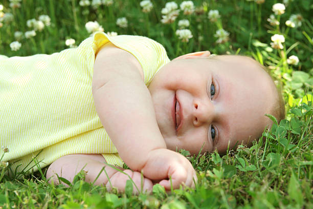 Sweet 3 month old newborn baby girl with a big smile as she lays down outside in the flower meadow on a summer day