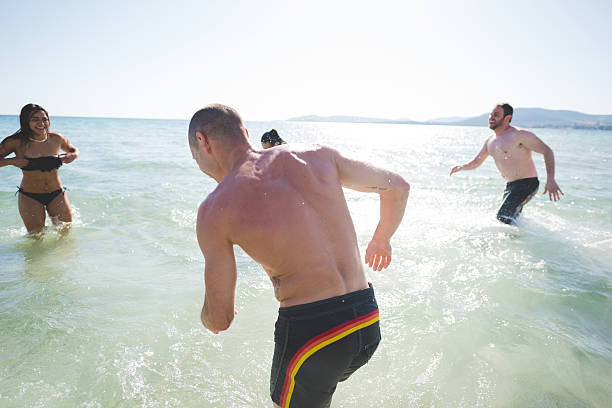 group of young multiethnic friends women and men at the beach in summertime having fun in the water splashing