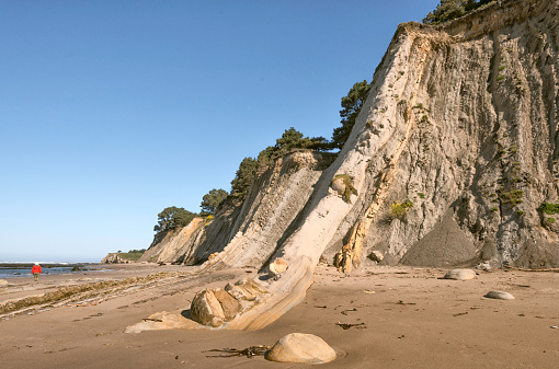 The cliffs in Northern California at Schooner gulch State Beach In Mendocino County,  and a solitary figure in red walking on the sand