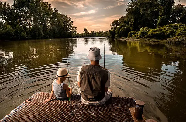 Photo of Rear view of a father and son fishing.