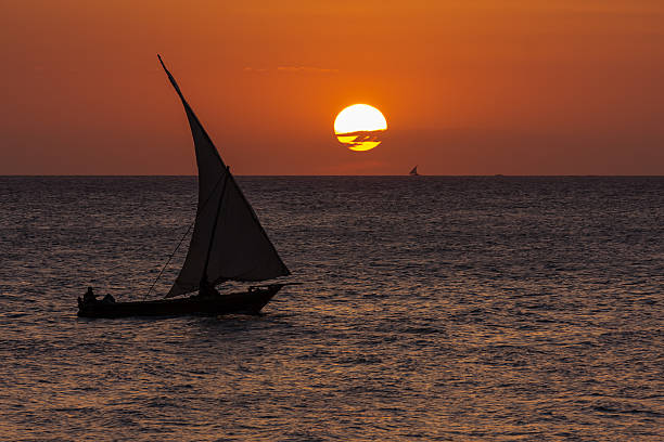 dhow a traditional african vessel used for fishing transporting cargo and people seen with the setting sun and a calm ocean of warm orange colors
