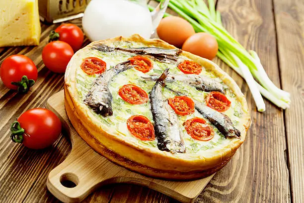 Quiche with sprats and cherry tomatoes on a wooden tableQuiche with sprats and cherry tomatoes on a wooden table