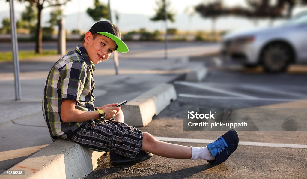 Boy Waiting for a ride in parking lot Boy Waiting for a ride in parking lot playing with phone 2015 Stock Photo