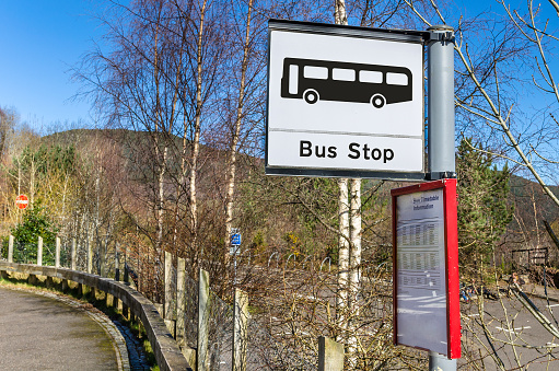 Bus Stop Sign in the Scottish Countryside. Leafless trees and mountains are visible in backgound.