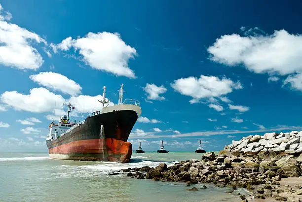 Cargo ship run aground on rocky shore waiting for rescue.