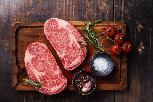 Two Raw fresh marbled meat Black Angus Steak Ribeye and seasonings on dark wooden background