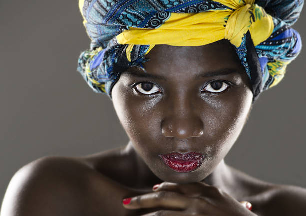Portrait of a black woman with a turban on her head. In the background the city at sunset