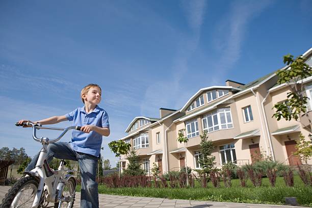 A father playfully chases his children on their bicycles on their driveway, the mother smiling on in approval.