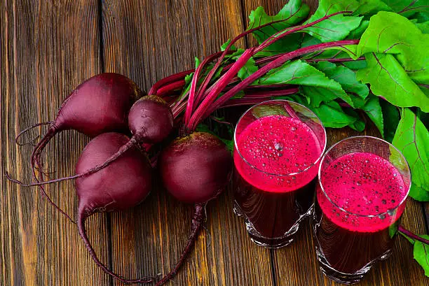 Glass of fresh beetroot juice with bets on wooden table.