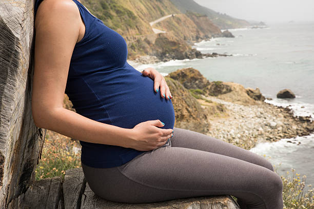 grávida mulher sentada no mar mantém seu estômago com amor - california highway 1 - fotografias e filmes do acervo