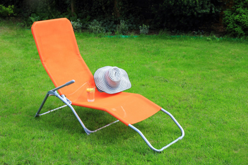 orange lounge sunbed standing on green grass in a private green garden