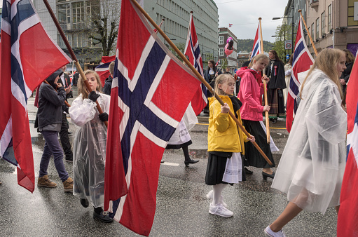 Bergen, Norway - May 17, 2015: School children - mostly school girls - are marching by (close to) the photographer in the Norwegian Constitution Day (May 17, Norwegian National Day) Celebration Parade (Hovedprosesjonen). The girls in the center of the image are holding large Norwegian Flags. It is raining lightly and most of the children are wearing raincoats.