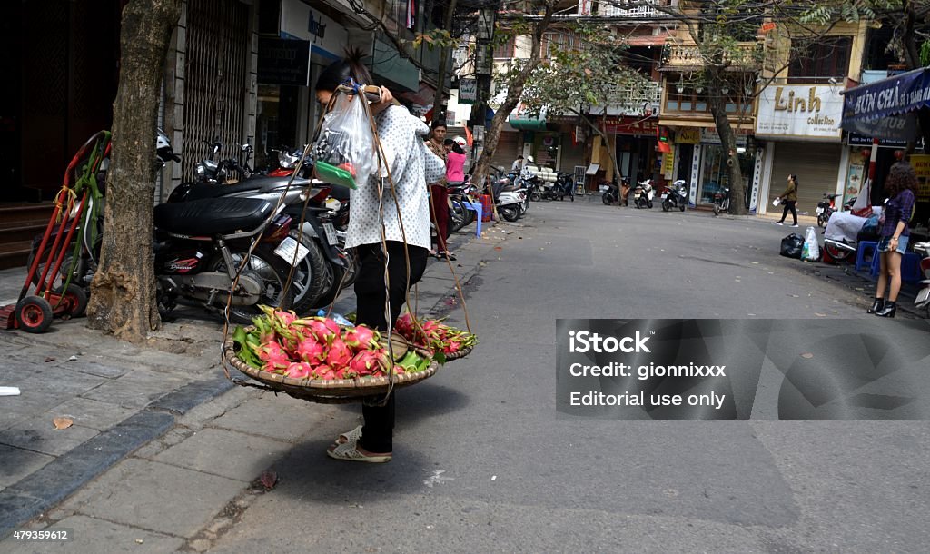 People on the street, Hanoi's old quarter, Vietnam Hanoi, Vietnam - February 24, 2015: Woman carrying fruit and girl wearing short pants in the background, on a street in the old quarter of Hanoi. Historical Hanoi's old quarter is always busy with people who comes for sightseeing and the nightlife.  2015 Stock Photo