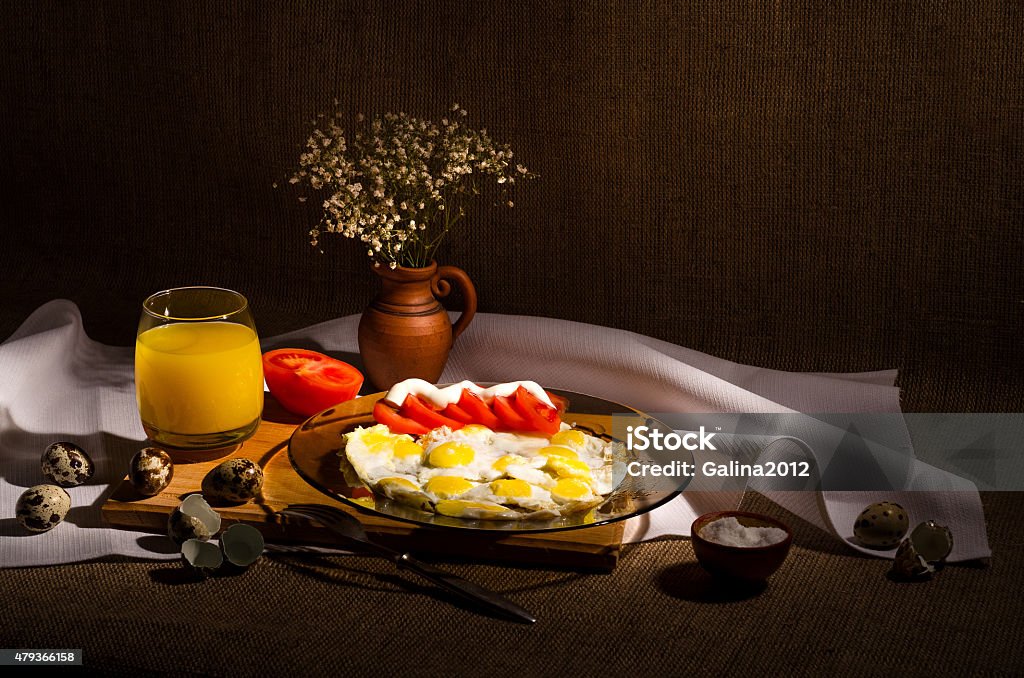 Fried quail eggs with tomatoes and mayonnaise Fried quail eggs with tomatoes and mayonnaise, on a plate. Juice in a glass and flowers in a vase. 2015 Stock Photo