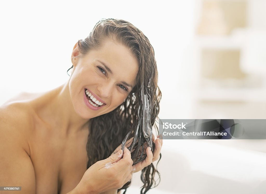 smiling young woman applying hair conditioner Smiling young woman applying hair conditioner Shampoo Stock Photo