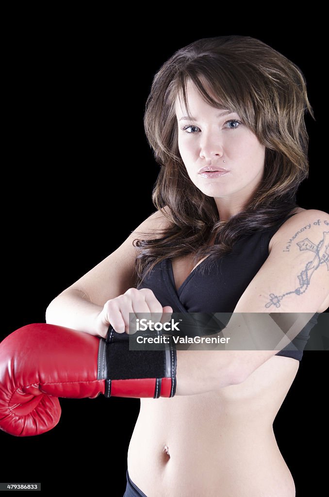 Female MMA fighter straps on glove while looking at camera. Vertical studio shot on black of young tattooed woman closing strap on red boxing glove while looking at camera. 20-29 Years Stock Photo