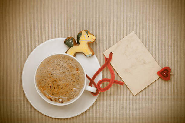 White cup of hot beverage drink coffee cappuccino latte with christmas handmade gingerbread cake pony dessert and blank paper card space for text message with red heart symbol love. Holiday concept.