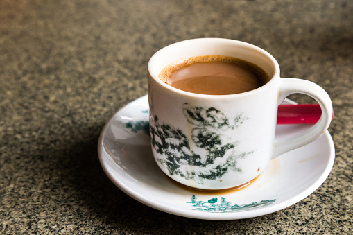 Traditional oriental Chinese coffee in vintage mug and saucer in soft focus setting with ambient light