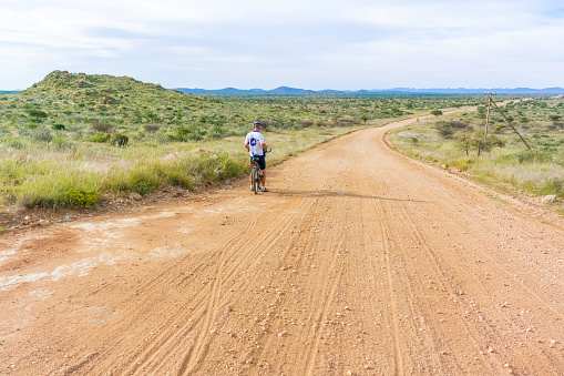 Khomas Highland, Namibia - April 24, 2015: Man on the bicycle on the road to Solitaire, Namib desert and Highlands landscape in Namibia.