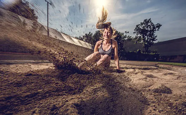 Young woman exercising long jumps and landing in a sand.