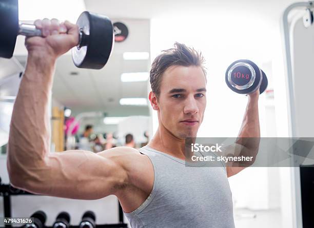 Young Man Exercising With Dumbbells And Looking At Camera Stock Photo - Download Image Now