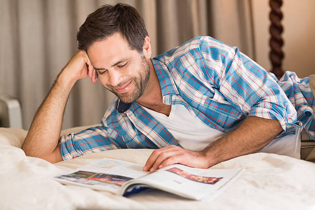 istock Handsome man relaxing on his bed reading magazine 479431736
