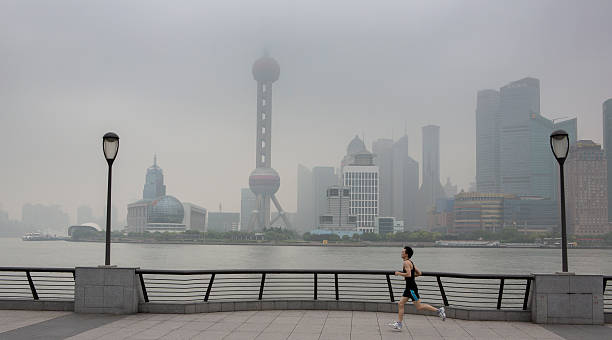 Pudong Smog viewed from Bund Promenade, Shanghai Shanghai, China - May 14, 2012: A jogger runs along the Bund promenade in Shanghai China. Across the Hangpu River behind him, the modern buildings of the Pudong district are obsured by smog. promenade shanghai stock pictures, royalty-free photos & images