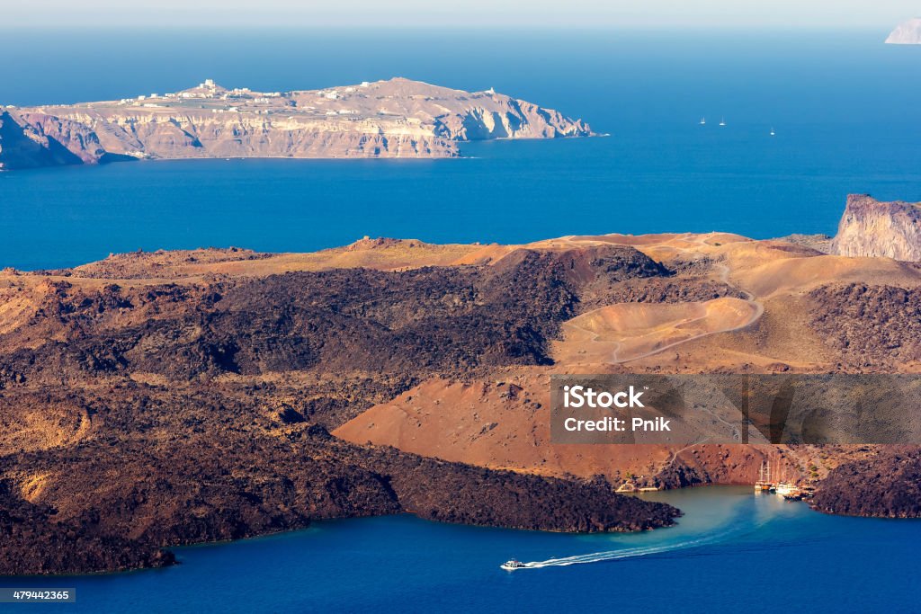 Volcanic island in Santorini Greece Nea Kameni volcanic island in Santorini Greece with little boat leaving the port photographed from a high point of view National Education Association Stock Photo