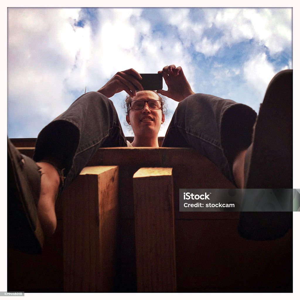 Man taking photo with cellphone A young man with dangling legs, sitting on a balcony and taking a picture with his cellphone. Shot with an iPhone. 2015 Stock Photo