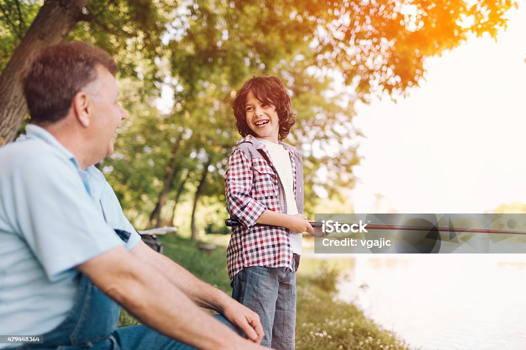 Grandpa and grandson fishing together. Grandpa and grandson fishing together on lake. Selective focus on smiling boy. Looking at his grandfather for support. 2015 Stock Photo