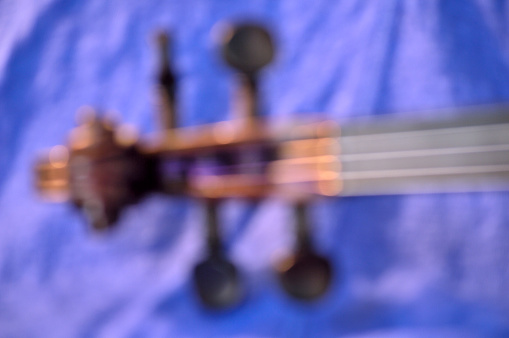 Modern bokeh abstract photo of dark-stained violin scroll against blue fabric background.