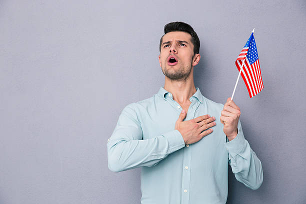 Patriotic young man holding US flag Patriotic young man holding US flag over gray background national anthem stock pictures, royalty-free photos & images