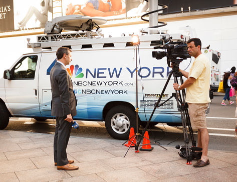 New York, New York, USA - June 29, 2015: An NBC TV reporter and his camera man in Herald Square in Manhattan. The are standing in front of an NBC broadcast van. Others can be seen in the background.