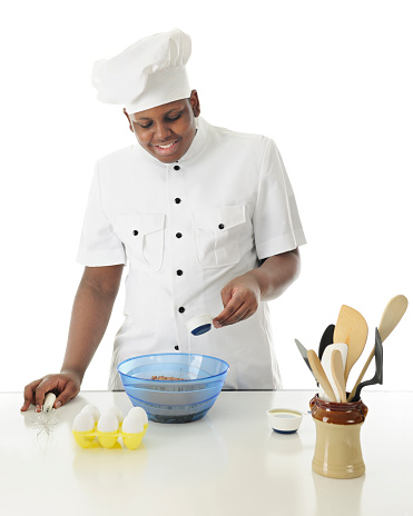 A young chef pouring a quarter cup water into the dry ingredients of a chocolate batter.  On a white background.