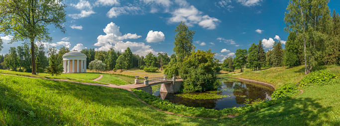 Summer park panorama with white classical rotunda and bridge over river